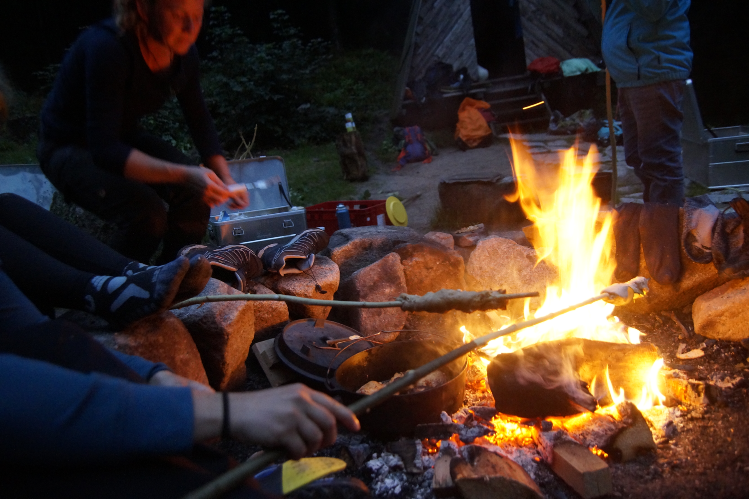 Menschen sitzen um ein Lagerfeuer und halten Stöcke mit umwickeltem Teich darüber. Foto: Daniel Müller