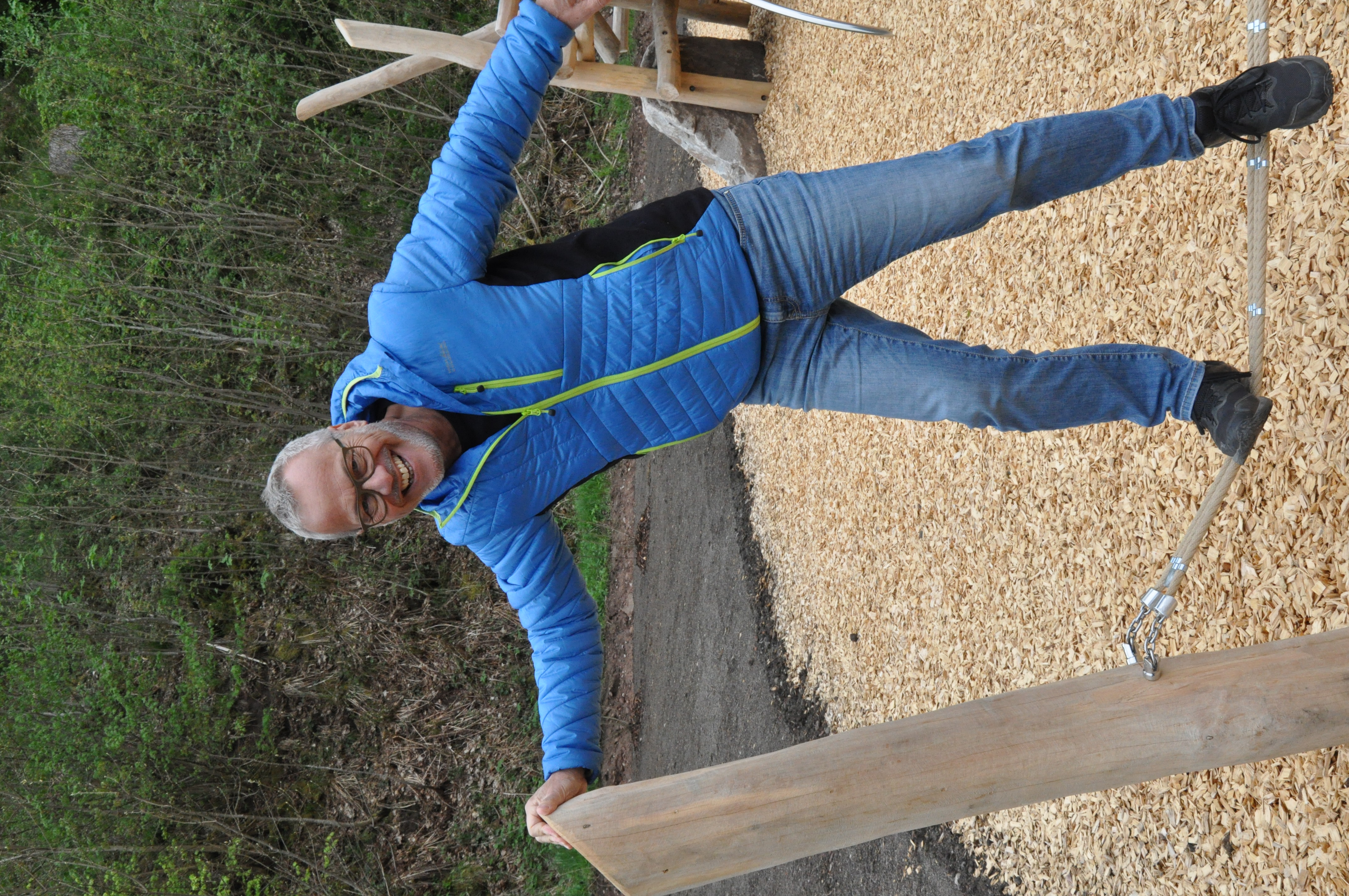 Ein Mann in blauer Jacke steht auf einem Spielplatz. Er testet ein Spielgerät.   