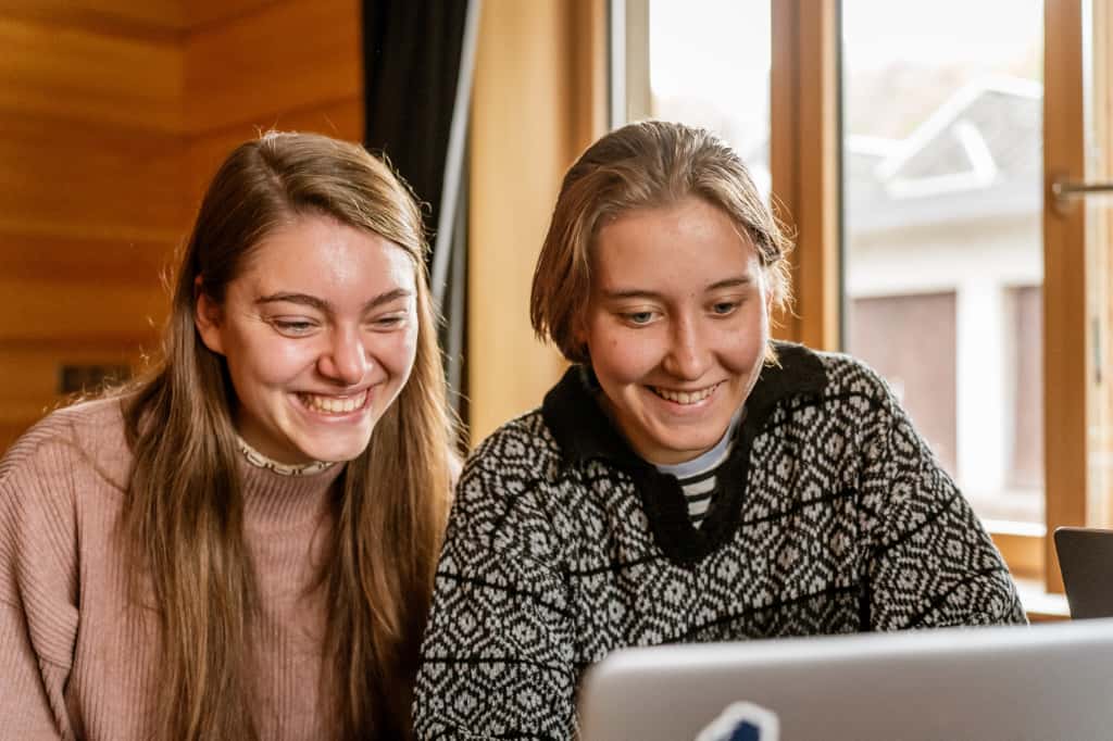 Zwei junge Frauen sitzen vor einem Laptop. Sie schauen auf den Bildschirm und lächeln. Foto: Abenteuer Schwarzwald
