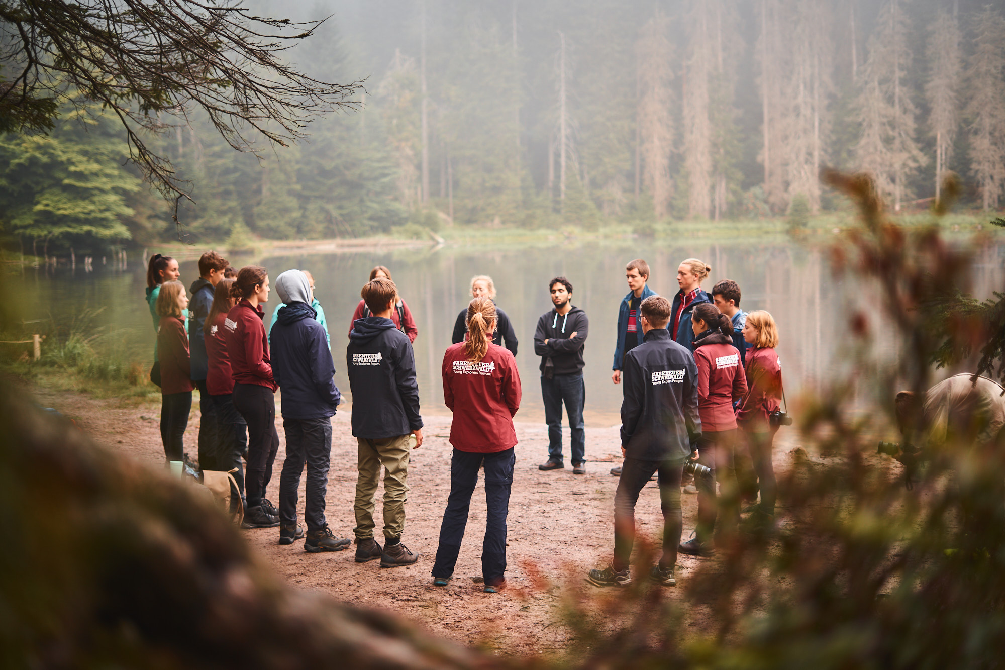 Eine Gruppe junger Menschen steht im Kreis. Hinter ihnen ist ein See. Sie tragen Oberteile mit der Aufschrift "Abenteuer Schwarzwald". Foto: Abenteuer Schwarzwald 