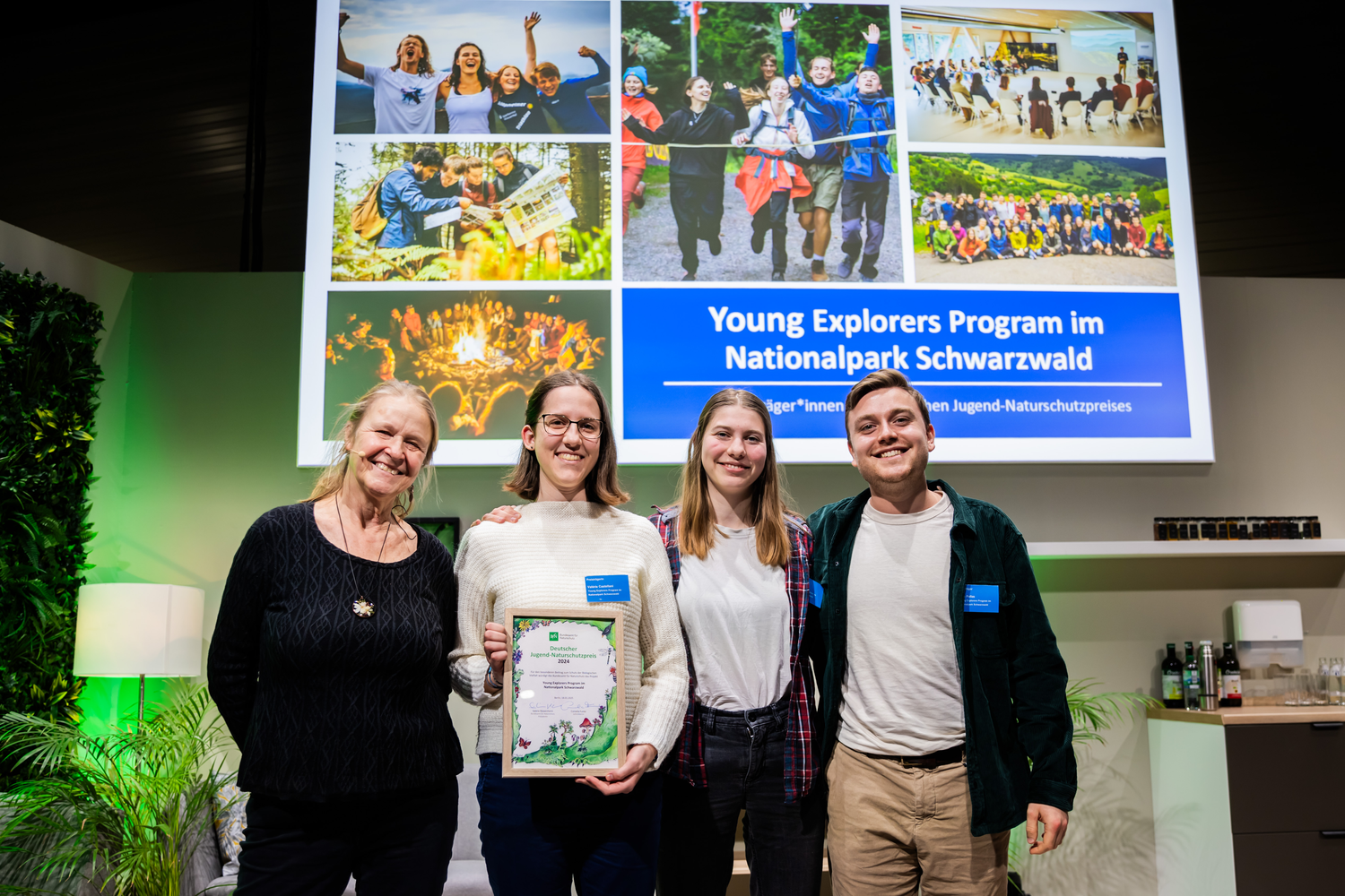 Eine ältere Frau, zwei junge Frauen und ein junger Mann stehen vor einer Fotowand, eine Frau hält eine Urkunde in den Händen. Foto: Christoph Soeder