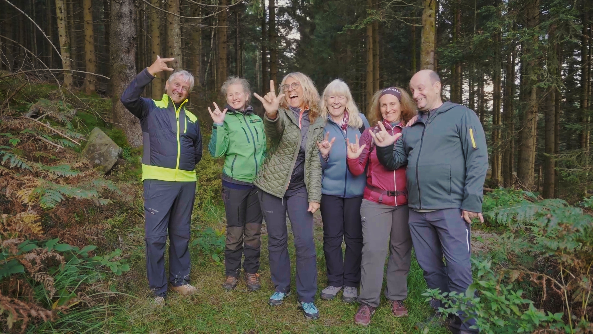 Eine Gruppe von sechs fröhlichen Wanderern (drei Frauen und drei Männer) steht nebeneinander auf einem Waldweg. Foto: Juliane Schrempp 